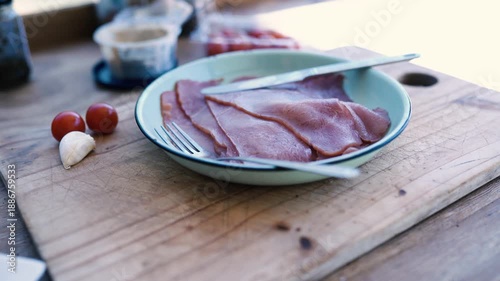Close-up shot of thinly sliced ham on a plate with fresh ingredients, with a rustic and appetizing appearance