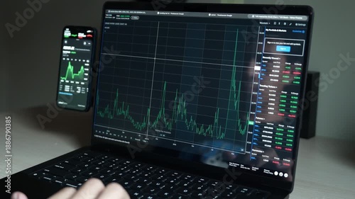 close up smartphone with laptop and open stock exchange, trading Online app interface. Man hand scrolling touch screen analysing chart forex crypto currency.