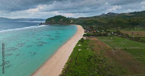 Wallpaper Mural Lombok Pantai Tomang Omang beach from above: curved sandy shore meeting turquoise water and green hills under cloudy sky, tranquil tropical bay perfect for travel and relaxation. Wild nature paradise Torontodigital.ca