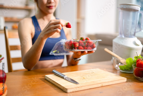 Healthy woman choosing fresh strawberries in kitchen for clean eating and fitness lifestyle. Concept of healthy snack, diet, nutrition, food preparation and wellness.