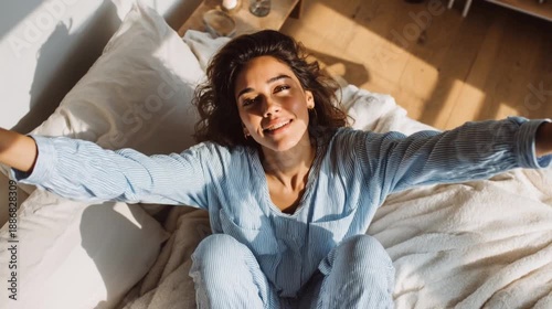 High-angle close-up shot of an attractive woman waking up and stretching joyfully in pajamas on a cozy sunny morning.