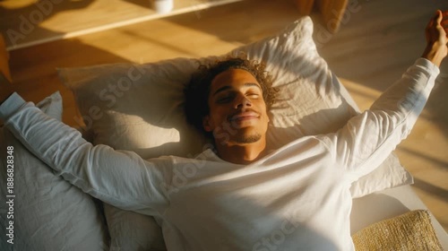 Happy Young Man Waking Up Stretching His Arms Relaxing on Bed in Warm Morning Sunlight