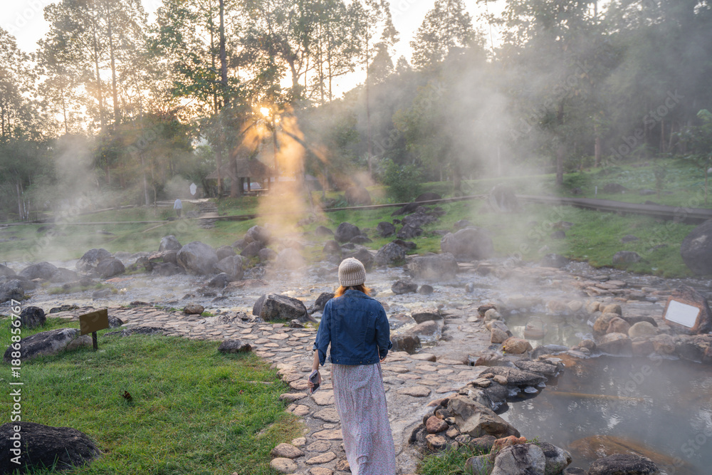 Obraz premium Woman Walking Along Stone Path at Steaming Natural Hot Springs in Thailand.