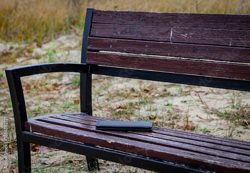 Tablou pe pânză Black leather wallet forgotten on a wooden park bench with a metal frame against
