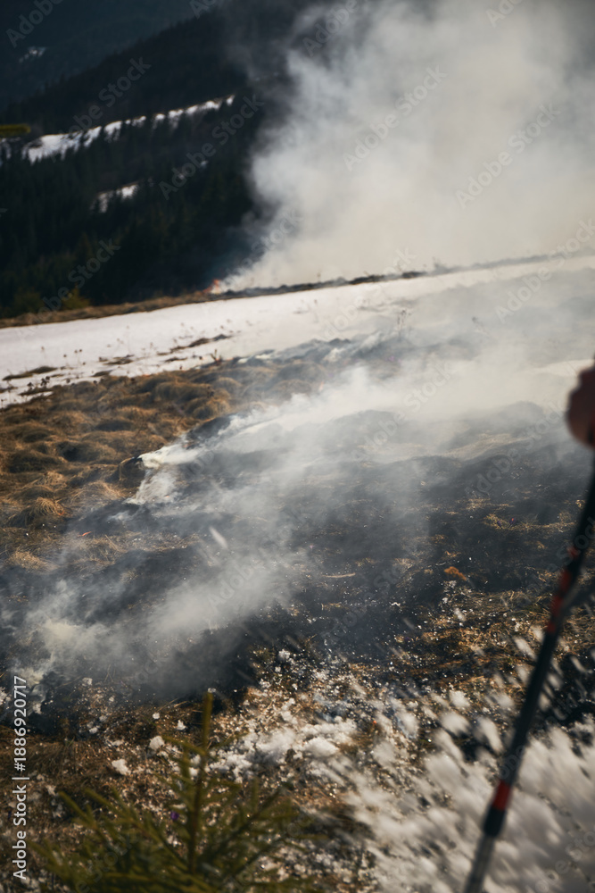 Fototapeta premium Forest fire. Fire burns grass and land near mountains with smoke rising into the air in a forest fire situation. Hiking in Carpathian Mountains, Ukraine