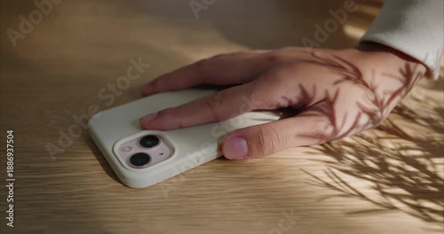 Minimalist morning routine. Detailed shot of a hand putting away a phone on a natural wood surface with soft sun flare. Symbolizing social media detox, mental health awareness, and the beauty of slow 