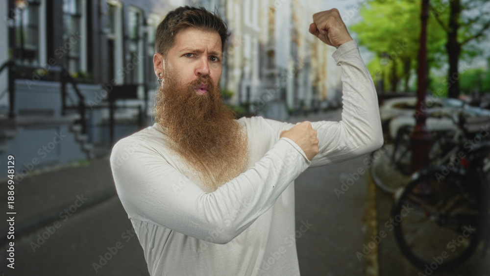 Fototapeta premium Bearded man in white shirt flexes bicep and grips muscle on city street with parked bicycles and trees; confidence.