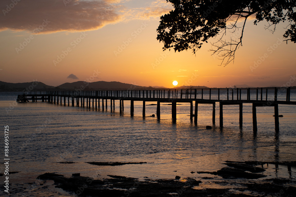 Obraz premium Silhouette of wooden pier stretching into the calm sea at golden sunset