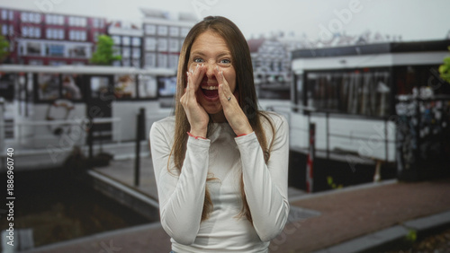 Photography Woman cupping hands to mouth on street in amsterdam with animated expression and open mouth, hands raised in calling gesture; excitement celebration