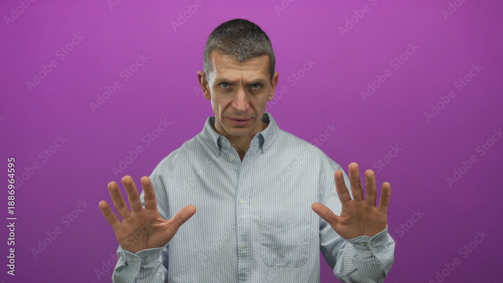 Naklejka premium Caucasian man in striped shirt makes calm gesture against vibrant pink background, exuding a sense of tranquility through expressive hand movements and focused demeanor.