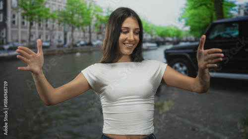 Photography Woman with outstretched hands and open arms on a street beside an amsterdam canal, smiling with palm forward gesture; welcome joy