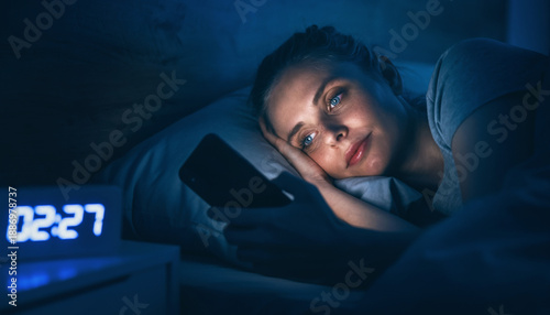 A woman lies awake in bed in the dark, illuminated by her smartphone screen, with a digital clock showing 02:27 AM on the nightstand.