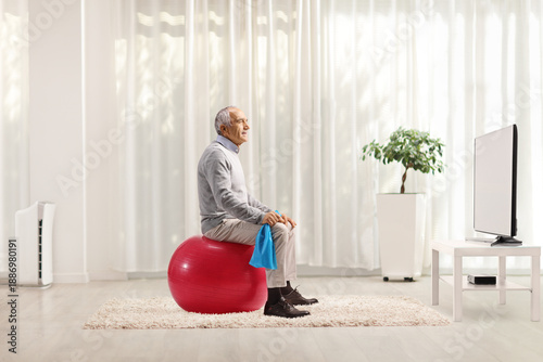 Φωτογραφία Active senior man sitting on a fitness ball at home
