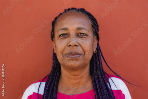 African senior woman with braided hair looking on camera with red background - Portrait of elderly person - Lifestyle and urban concept