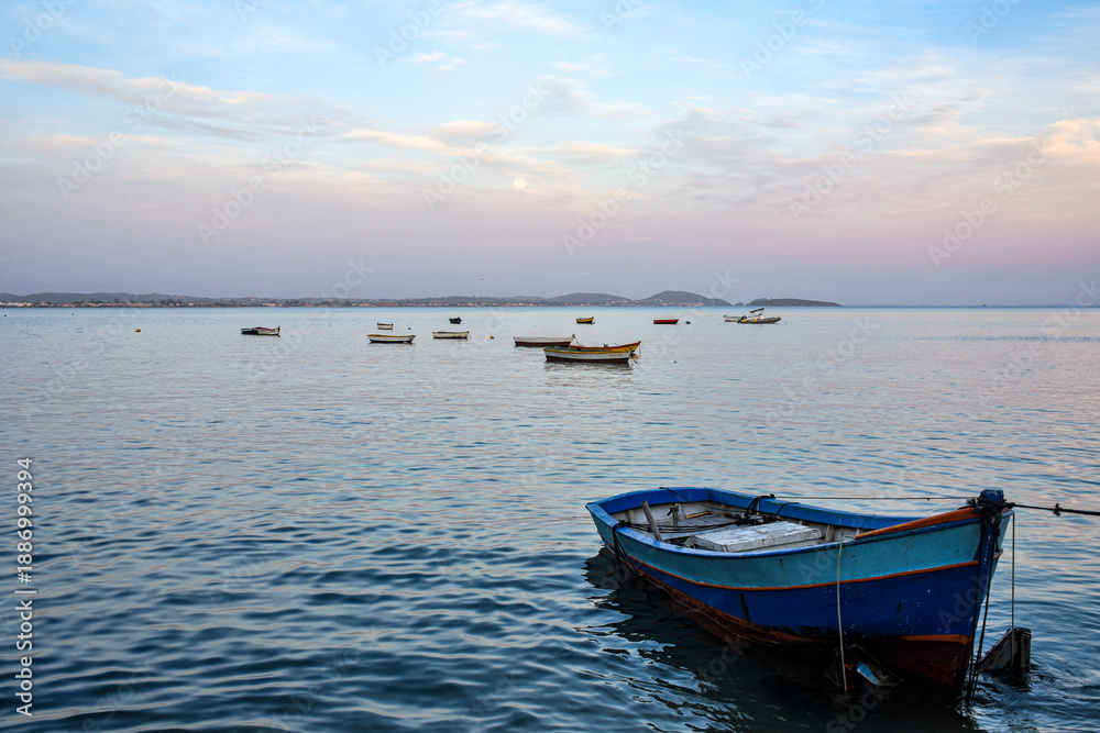 Naklejka premium Blue wooden fishing boat anchored in calm sea at twilight with pastel sky