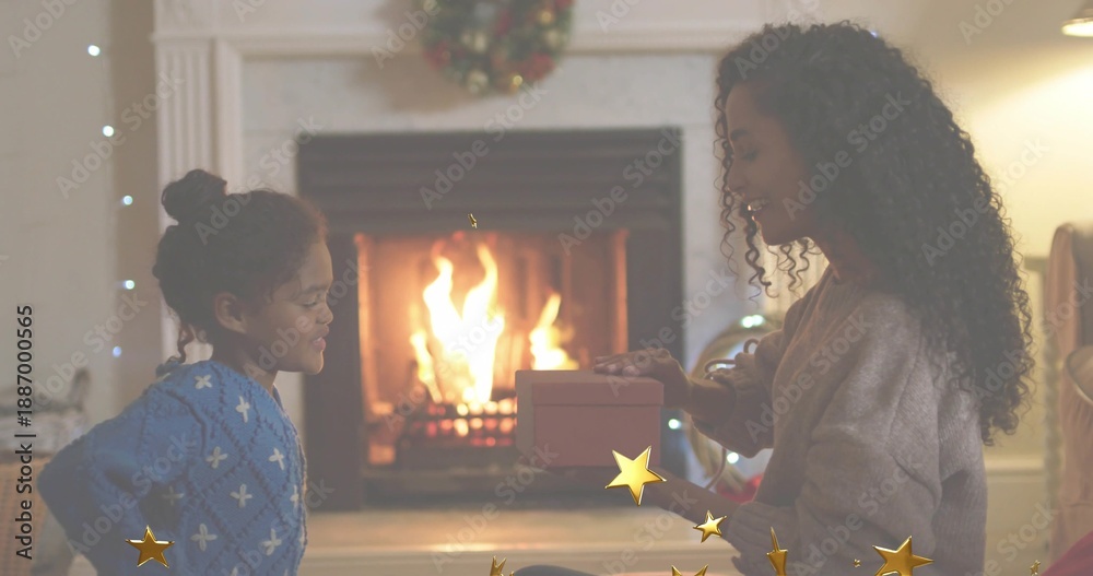 Obraz premium Handing woman presenting wrapped gift to child in blue sweater in living room by lit fireplace