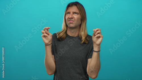 Man with long blond hair making finger quotes gesture with both hands and a skeptical expression in a studio; skepticism humor.