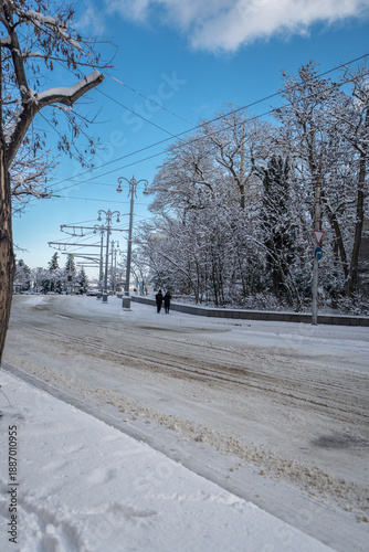 Winter city street. Roads, sidewalks and trees are heavily covered with snow. A sunny January day. After a heavy overnight snowfall. New Year's Morning. An empty road.