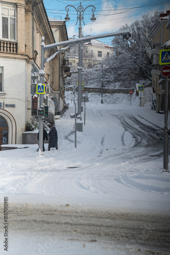 Winter city street. Roads, sidewalks and trees are heavily covered with snow. A sunny January day. After a heavy overnight snowfall. New Year's Morning. An empty intersection. People on a walk.