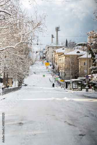 Winter city street. Roads, sidewalks and trees are heavily covered with snow. A sunny January day. After a heavy overnight snowfall. New Year's Morning. An empty road. People on a walk. Old buildings