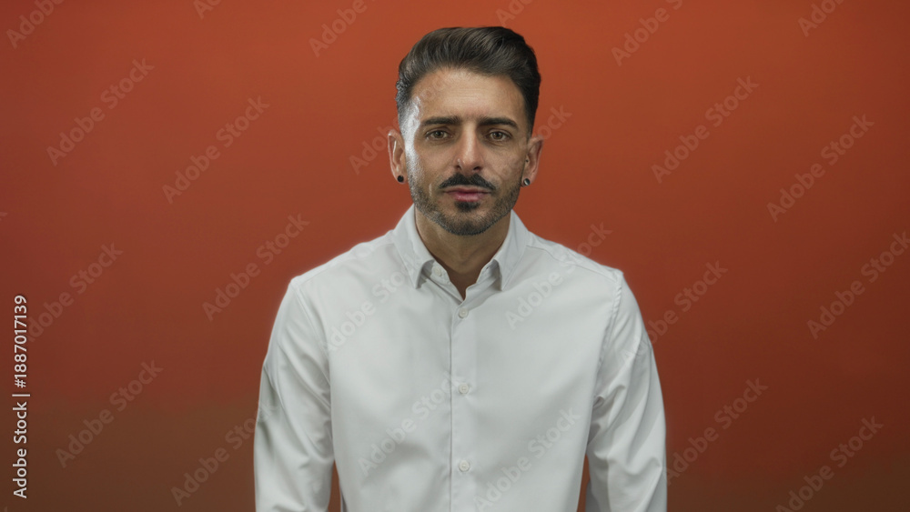 Obraz premium Man with uncovered face and white shirt looking directly at camera in bright orange studio; confidence.