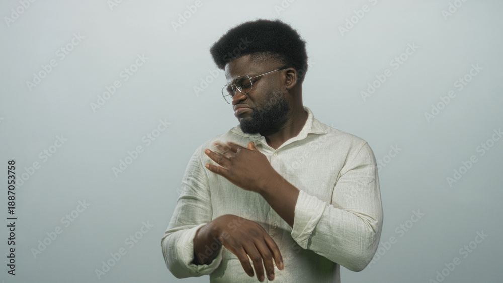 Obraz premium Man adjusts glasses, tugs shirt collar and frowns while squinting at camera in studio against pale gray wall; annoyance.