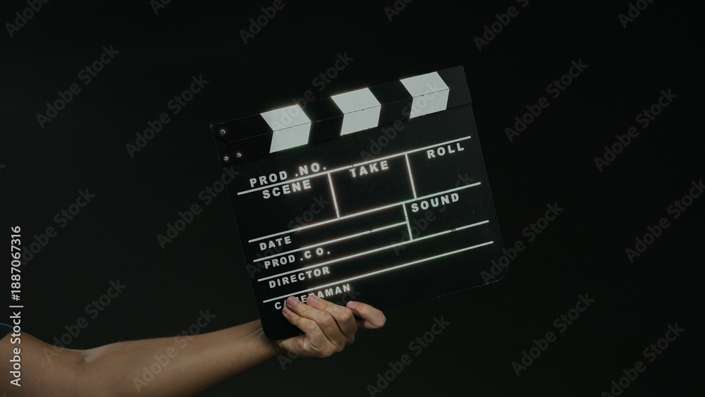 Naklejka premium Man holding film clapperboard against black background signifies filmmaking and production process.