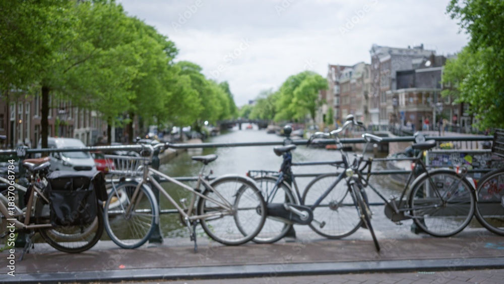Fototapeta premium Bicycles parked on a bridge in amsterdam with a blurred view of canals and historic buildings under a cloudy sky captured in a defocused aesthetic.