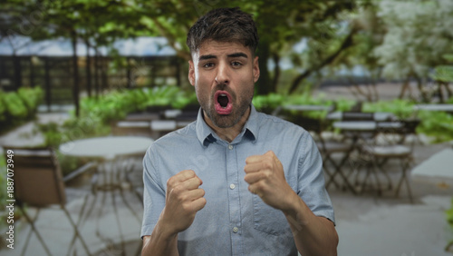 Photography Young hispanic man shouting and clenching fists on sunlit outdoor restaurant terrace; victory pride