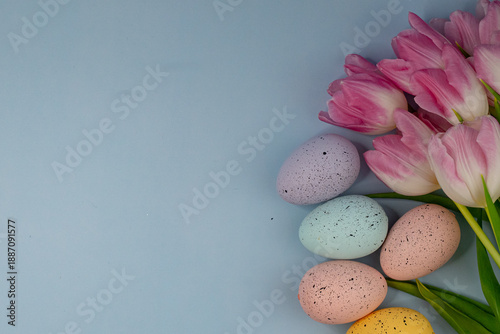 Pastel-colored Easter eggs arranged with pink tulips on a soft blue background. Minimal spring holiday flat lay with copy space for seasonal design