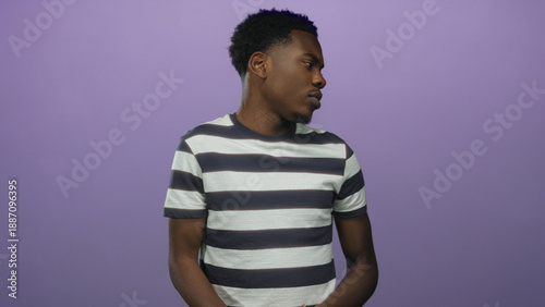 Foto Man wearing striped shirt turns head to side revealing facial expression in purple studio; contemplation