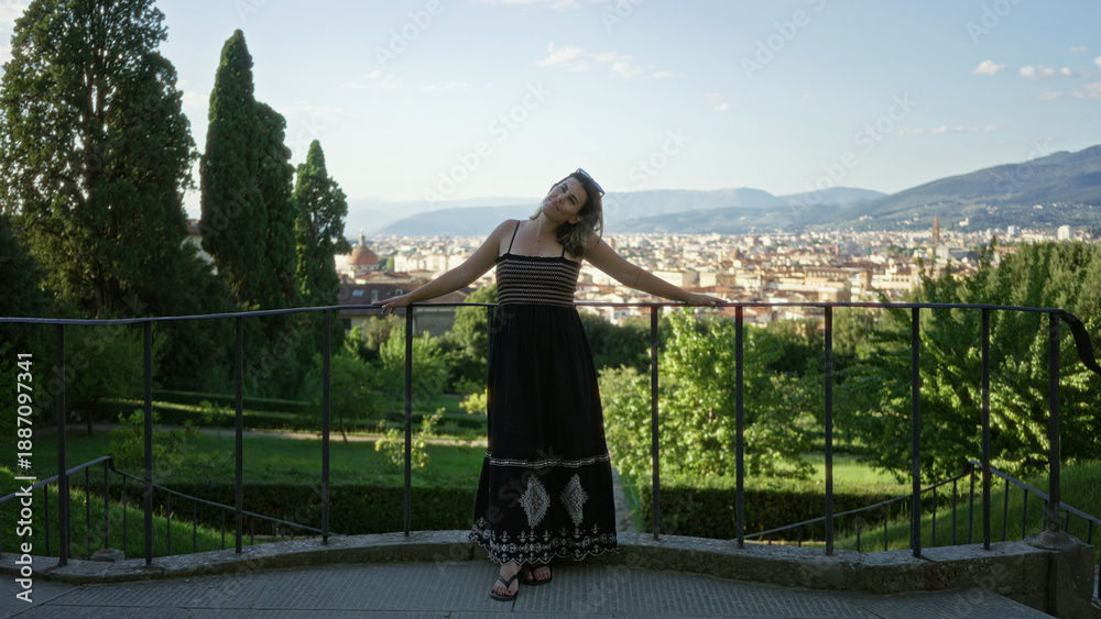 Naklejka premium Woman with bare arms resting on an iron railing, looking out over florence city buildings from a viewpoint overlooking rooftops and hills; serenity.