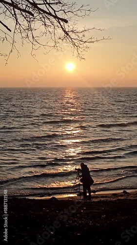 A silhouette photographer capturing images by the sea at sunrise