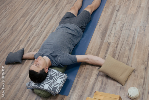 Photography Man doing shavasana laying on yoga mat and bolster with weights on his palms, re