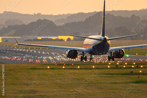 Aircraft taxiing on runway with illuminated lights at airport during early evening hours