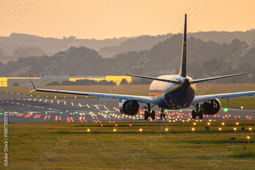 Landing aircraft at runway with illuminated markers and distant hills in view