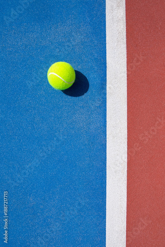 Single tennis ball resting on a blue outdoor court.