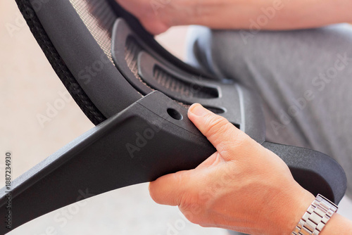 A person assembling the backrest and arms of an office chair. Furniture assembly at home