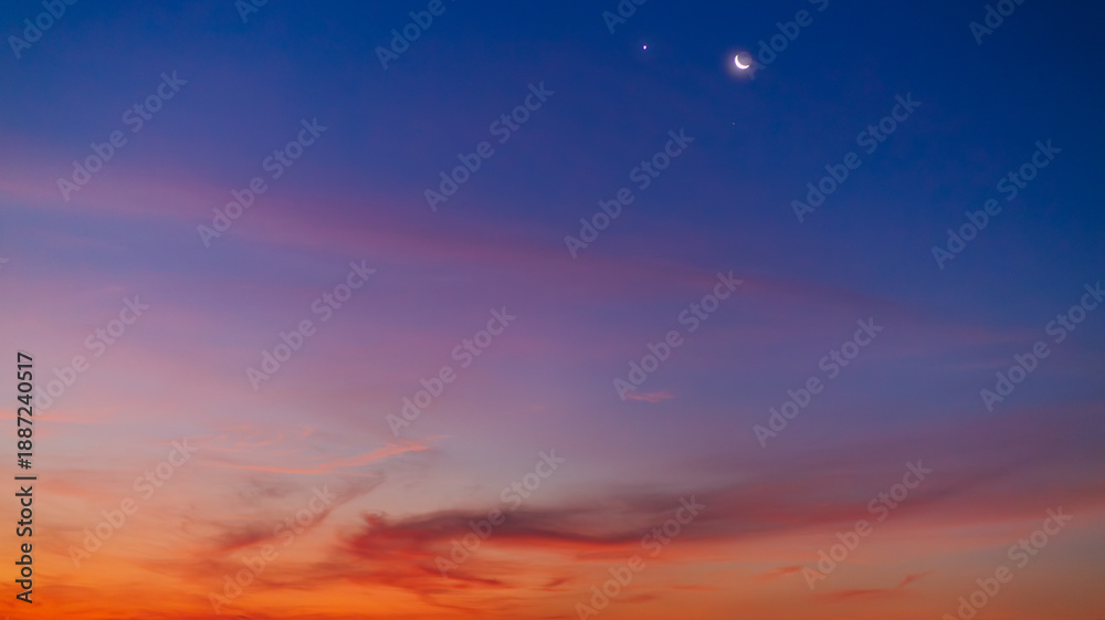 Fototapeta premium Crescent Moon and Planets in the Twilight Sky Over Soft Sunset Clouds,A breathtaking view of a thin crescent moon shining alongside bright planets in a deep blue twilight sky. The lower horizon.