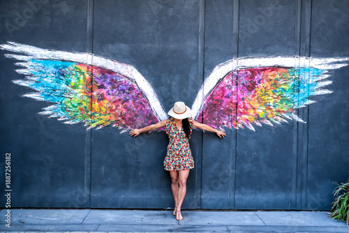 A woman stands in front of a mural of a winged angel
