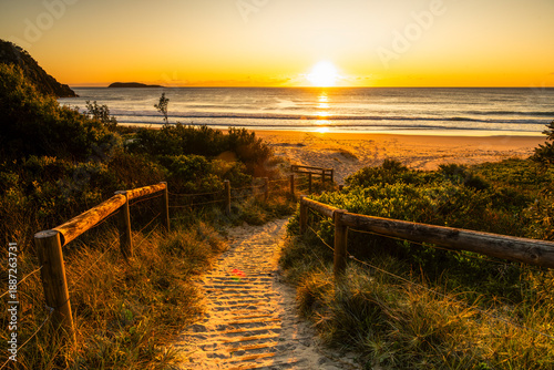 Golden sunrise over Zenith Beach in Port Stephens, Australia, with a sandy path leading to the ocean, showing calm coastal scenery and early morning light.