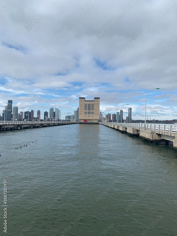 Fototapeta premium Brooklyn Bridge Park pier house control tower rising from waterfront piers amid Manhattan skyline towers under partly cloudy gray skies over East River