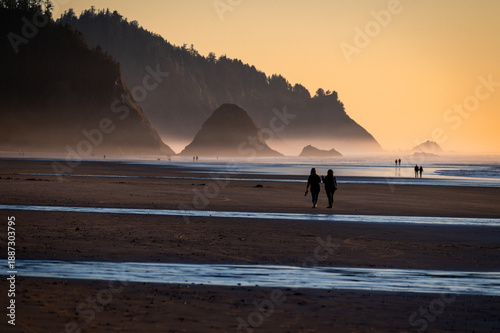 Silhouette of people beach walking during a beautiful sunset along the Oregon coast at Arch Cape. Nothing more enjoyable than walking a wide sandy beach during a glorious sunny evening in Oregon.