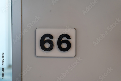 White room number 66 sign black numerals wall mounted
