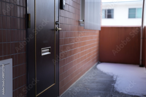 A brick wall with a brown door and a window. The door is closed and the window is open