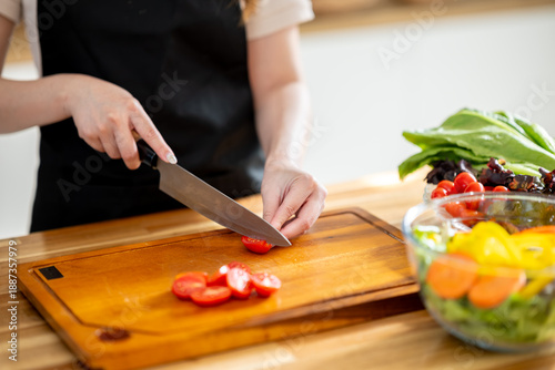 An Asian woman is slicing tomatoes on a kitchen table to make a salad. The imagery relates to healthy eating and dieting.
