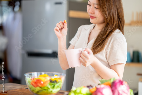 An Asian woman is taking vitamins in the kitchen. The concept of healthy eating and dieting.