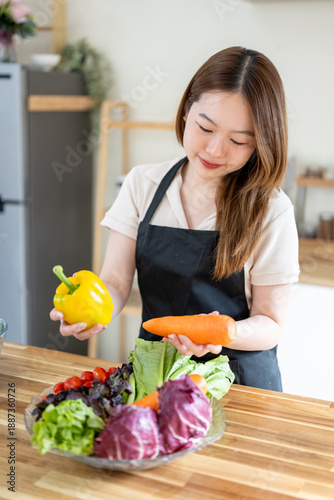 An Asian woman is arranging vegetables on a plate on a kitchen table, promoting the concept of healthy eating and dieting.