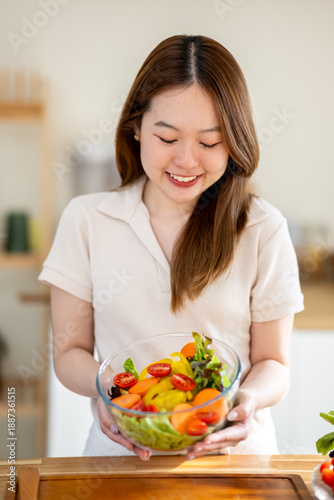 An Asian woman is making a salad in the kitchen. The concept is related to healthy eating and dieting.