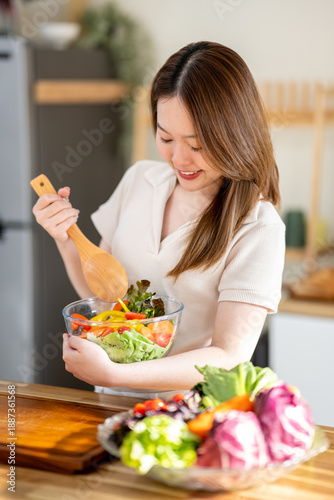 An Asian woman is making a salad in the kitchen. The concept is related to healthy eating and dieting.